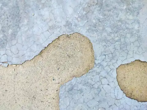 A pale coating on concrete, cracked into a fine web and peeled away in patches, seen from above