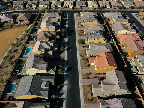 Two-story stucco houses with concrete tile roofs, backyard pools and gravel yards along a street, seen from above