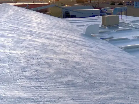 The rippled white surface of a coated spray foam roof, with skylights and ductwork beyond it