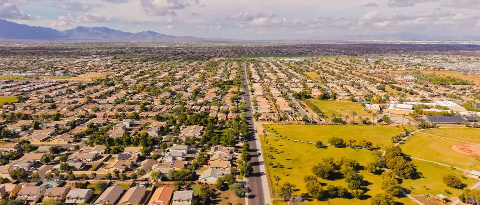 An Arizona suburb seen from the air, with rows of tile-roofed houses along a straight road, a park and mountains in the distance