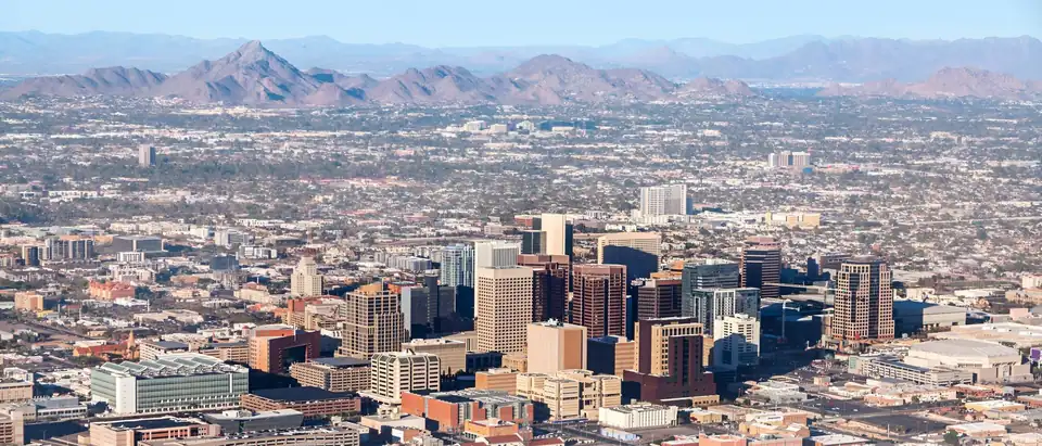 Downtown Phoenix seen from the air, with flat-roofed buildings in the foreground and desert mountains behind the towers